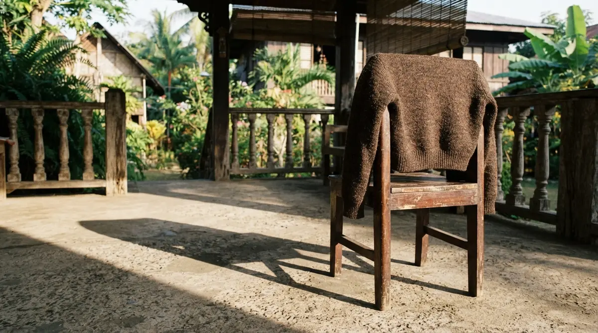 A thick sweater hangs on a wooden chair on a sunny, shaded veranda.