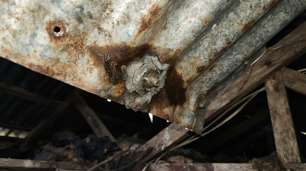 Water stain spreading from a metal mounting bolt on a corroded corrugated iron roof.